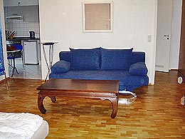 a wooden floor, double couch nd a table in the living/sleepingroom
